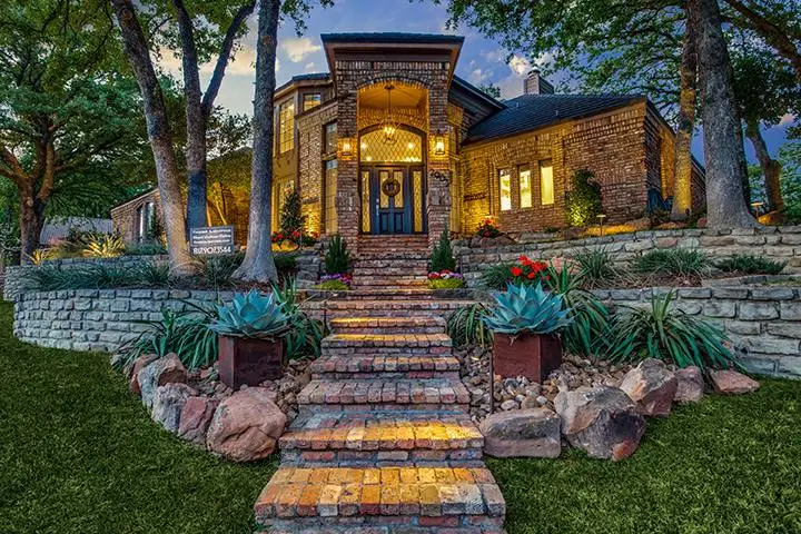 Lit stone steps and garden beds leading to a brick home entry in Arlington, TX