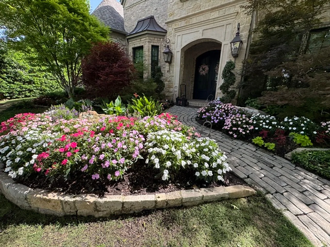 Stone-edged flower beds lining a paver walk to a stone home entry